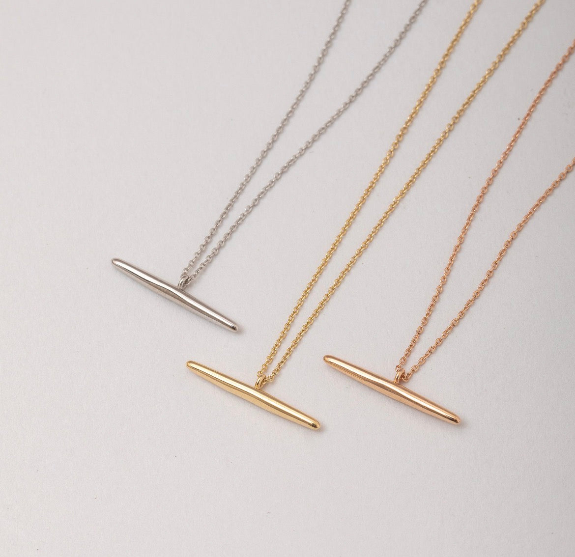 14k solid gold T-bar necklace in yellow gold, rose gold, and silver, flat lay on white background
