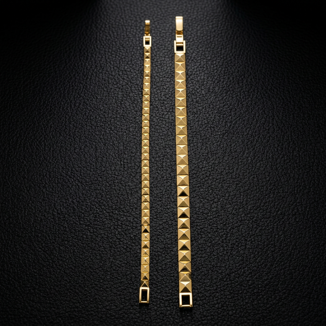 Small and large 14k yellow gold pyramid stud bracelets laid side by side on a black background, showing their different widths and latch closures.

