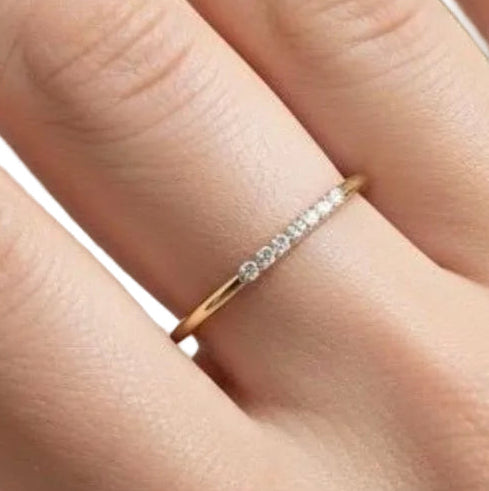 Dainty gold diamond stack ring worn on a finger, showing the slim band and delicate row of diamonds.
