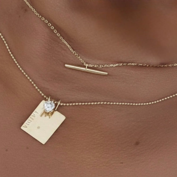 14k solid gold T-bar necklace layered with gold chain necklaces on model
