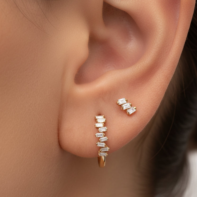 14k solid gold staggered diamond baguette huggie earring styled with triple baguette diamond stud on ear
