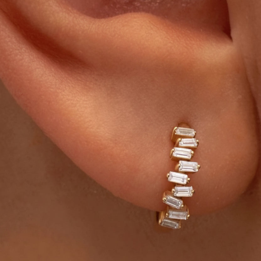 14k solid gold staggered diamond baguette huggie earring worn on ear, close-up
